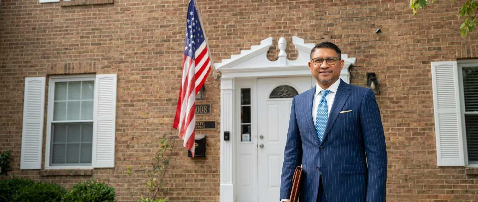 A person in a business suit standing outside a brick building with an American flag in Fairfax, Virginia